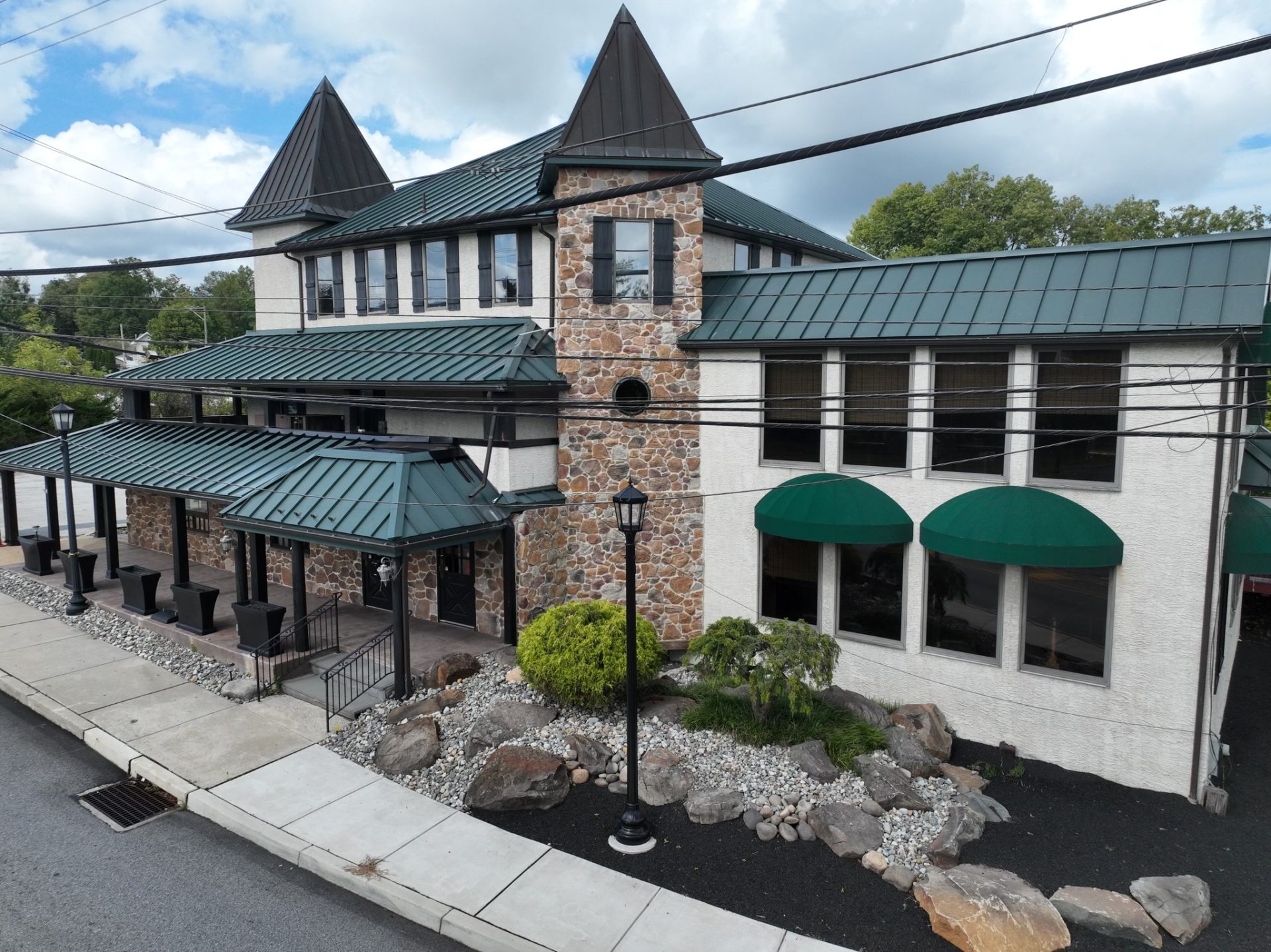 Stone building with green metal turret roofs and a landscaped stone garden bed in Collegeville, Pennsylvania